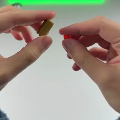 Hands press a red toy dart into a gold shell