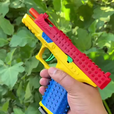 A hand pulls back the red slide of the Brick Blaster